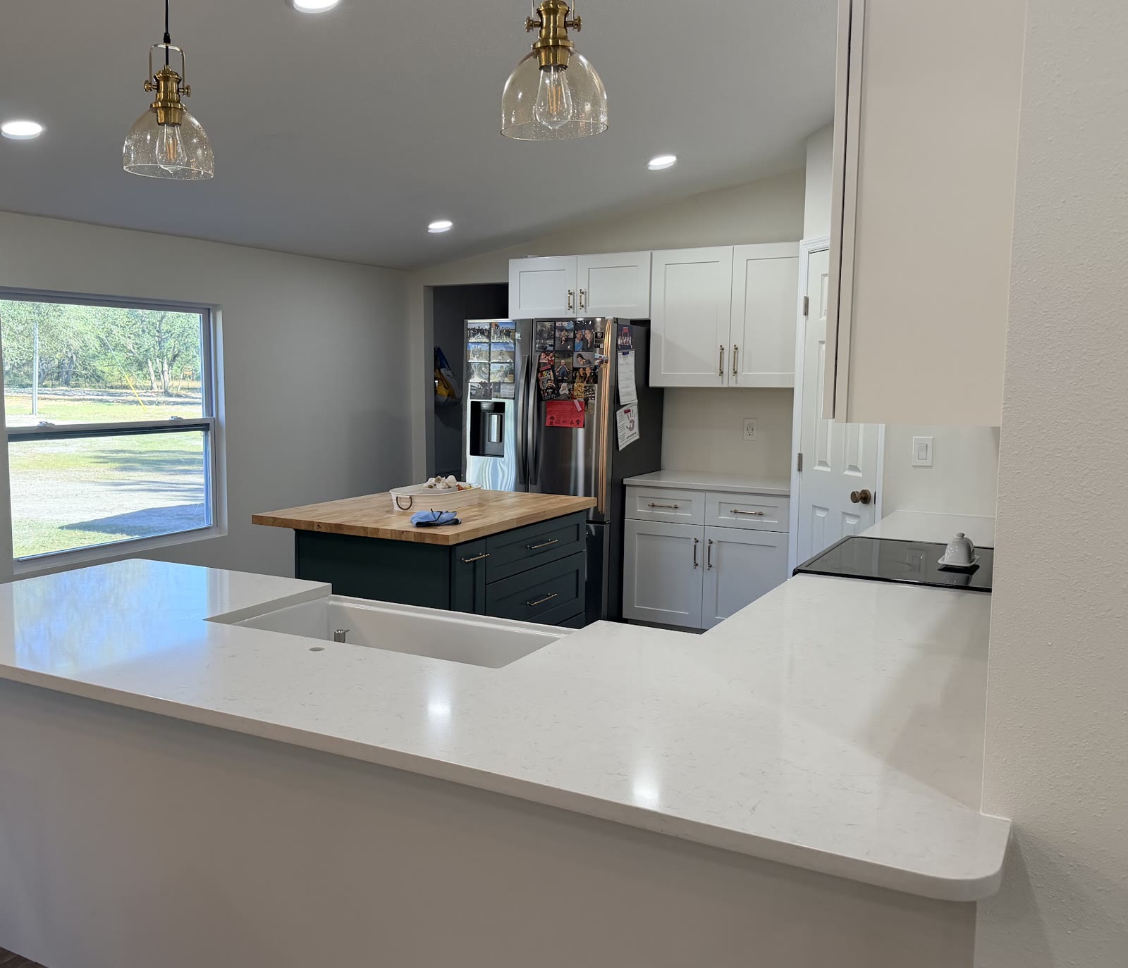 A remodelled kitchen with a white quartz peninsula, butcher-block island, shaker cabinets and brass pendant lights.